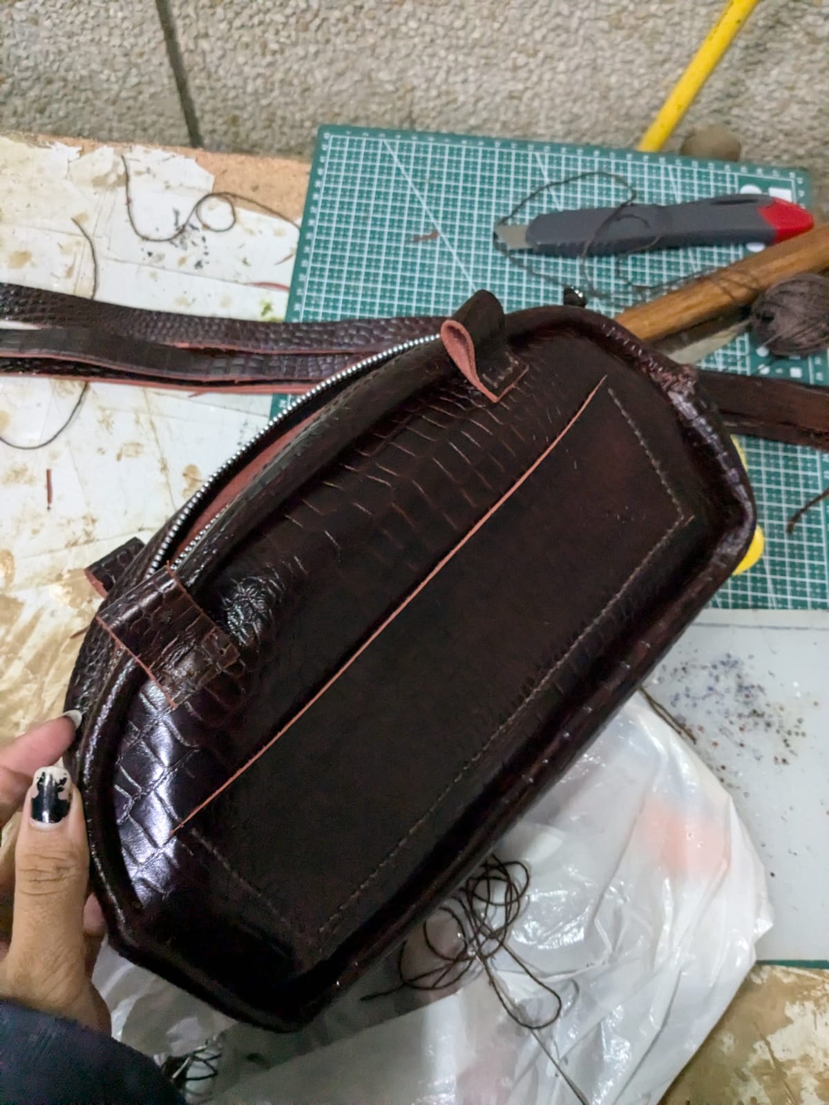 Top view of the leather purse during construction with tools and stitching materials nearby